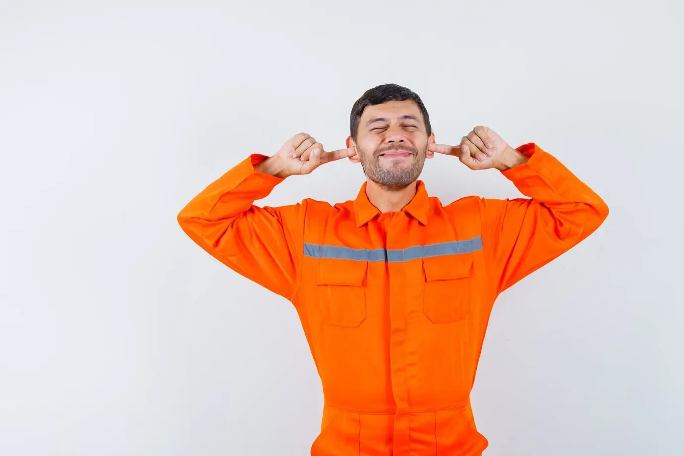 Ouvrier industriel en uniforme se bouchant les oreilles avec les doigts et ayant l’air agacé, vue de face.